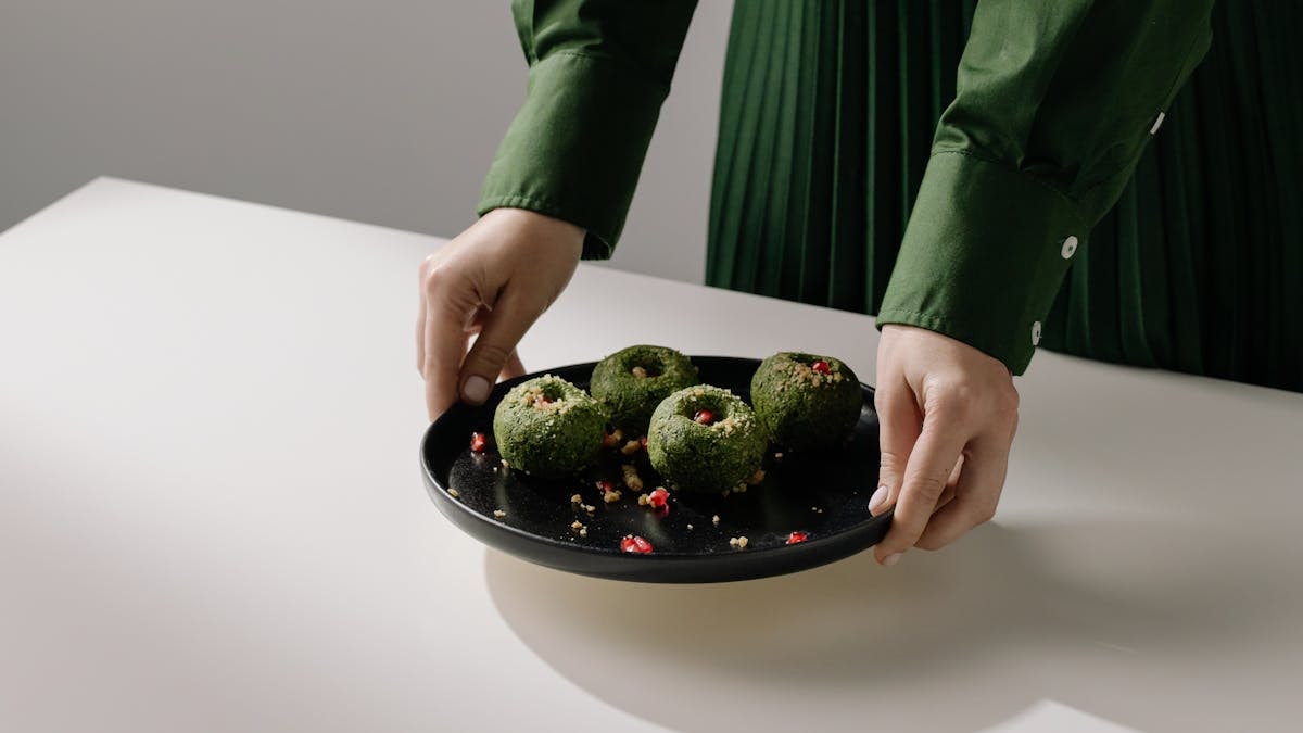 Hands presenting a black plate with spinach pkhali, showcasing traditional Georgian vegan cuisine.